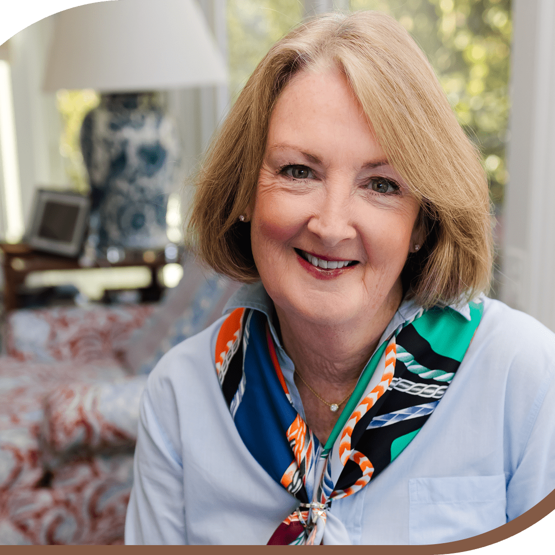 Smiling woman with blonde hair and colorful scarf in cozy indoor setting.