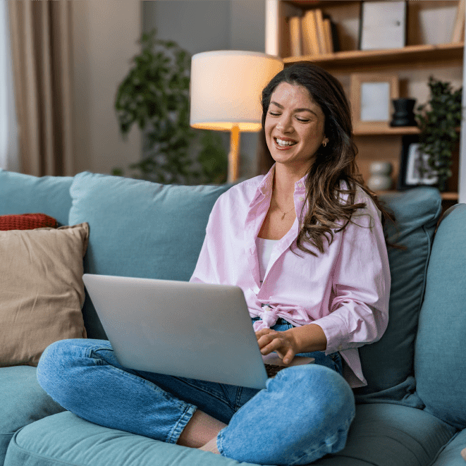 Woman smiling while using laptop on couch.